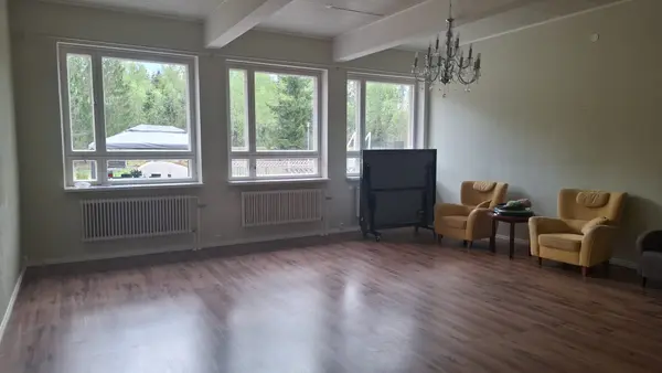Tilava yhteinen oleskelutila — suuret ikkunat, kattokruunu ja nojatuolit